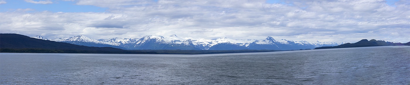 Snow-capped mountains rise majestically over a calm body of water under a partly cloudy sky