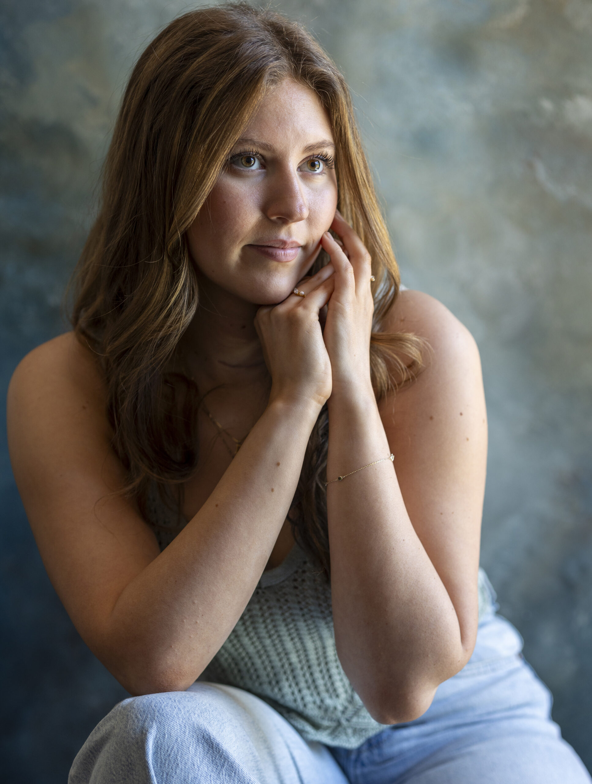 A young woman with long brown hair gazes thoughtfully while resting her chin on her hands