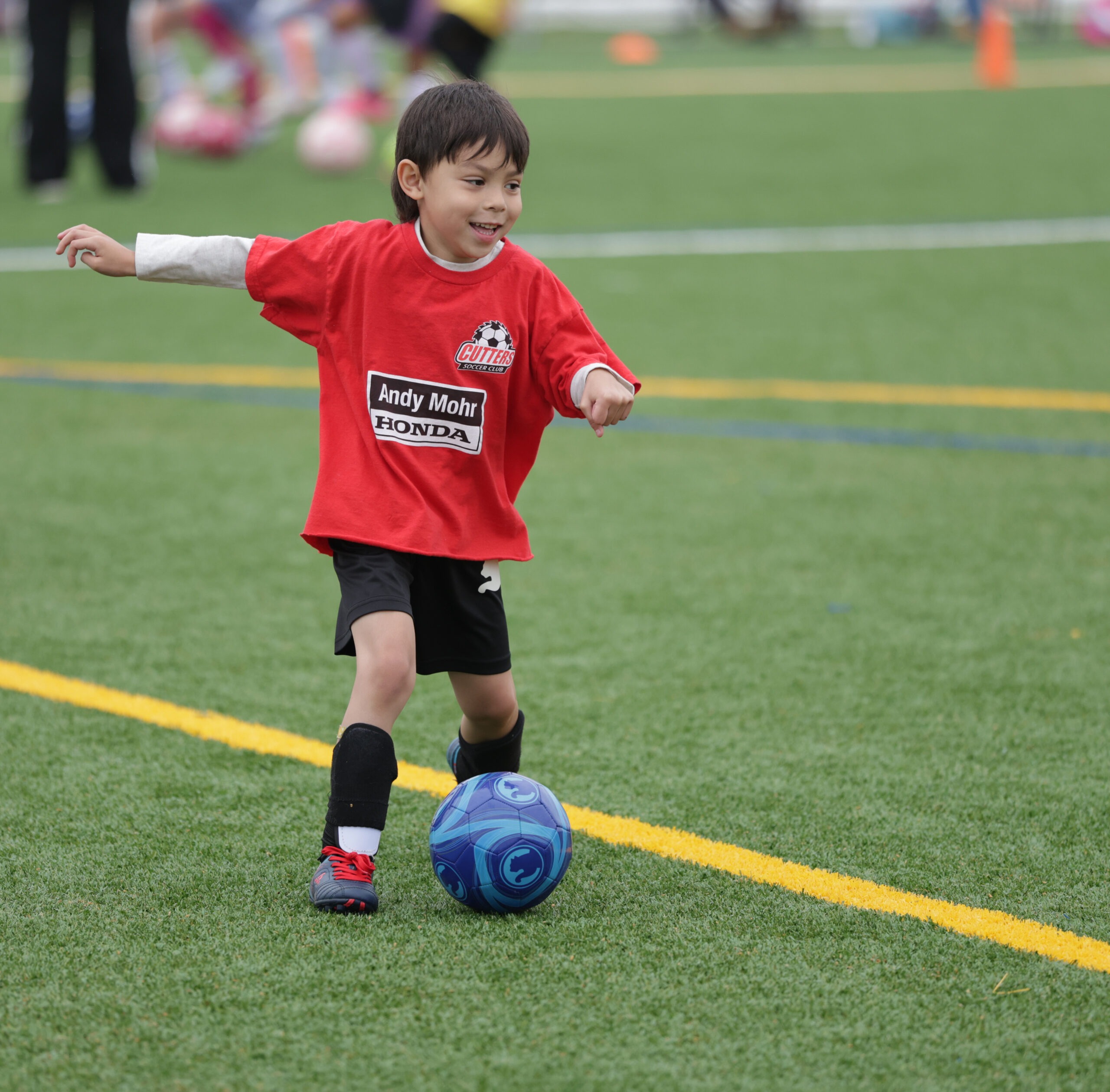 A young boy in a red soccer jersey kicks a blue ball