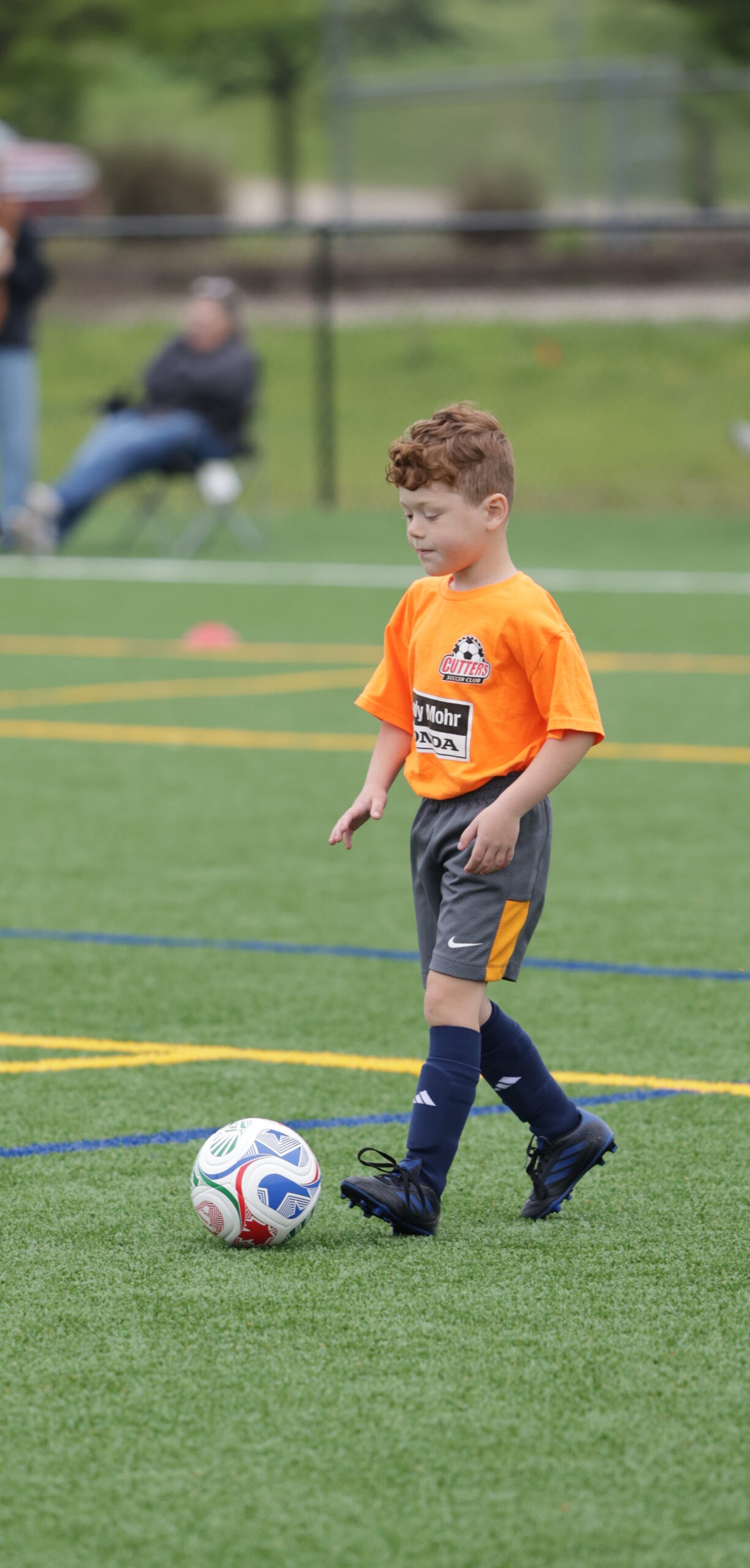 oung boy in an orange soccer jersey stands on a field,